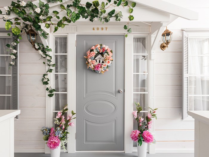 Neutral colored front porch decorated with greenery and pink flowers. 